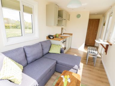 A small living area with a gray sectional sofa and green pillows next to a compact kitchen with wooden countertops at Malvern View Lodge in Wadborough near Pershore