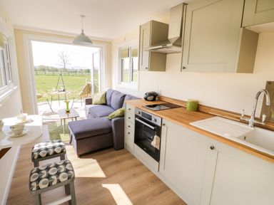 A kitchen and living area with wooden countertop oven sofa and stools leading to an outdoor seating area at Malvern View Lodge in Wadborough near Pershore