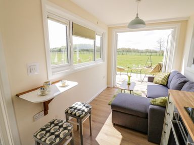 A small living area with a sofa table with cups stools and an open door leading to a patio and field at Malvern View Lodge in Wadborough near Pershore