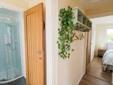 A hallway with a shower room door open on the left and a bedroom visible on the right with a coat rack and hangers on the wall in between at Malvern View Lodge in Wadborough near Pershore