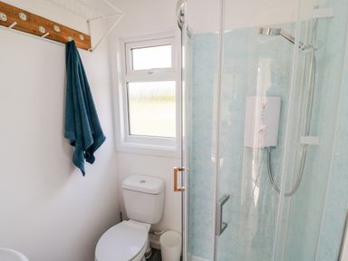 A bathroom with a toilet a blue towel on a wooden hook rack and a glass shower enclosure at Malvern View Lodge in Wadborough near Pershore