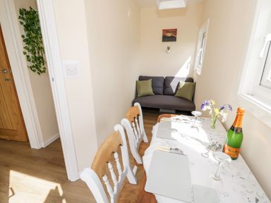 A dining area with a table set for two next to a small sofa with green cushions at Malvern View Lodge in Wadborough near Pershore