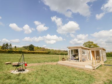A wooden lodge with outdoor seating and a fire pit in a grassy field at Malvern View Lodge in Wadborough near Pershore