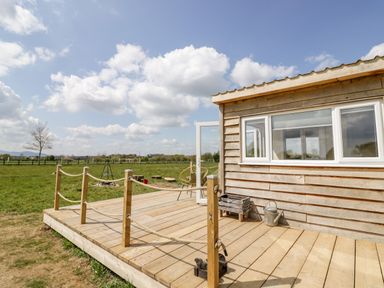 A wooden deck attached to a wooden cabin with rope railing and an open door overlooking a grassy field at Malvern View Lodge in Wadborough near Pershore