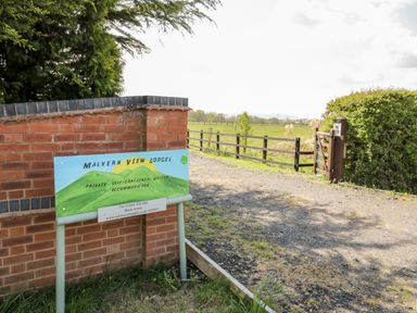 A driveway with a wooden gate and a sign for Malvern View Lodges on a brick wall at Malvern View Lodge in Wadborough near Pershore