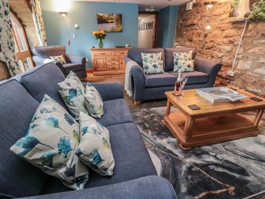 A sitting room with sofas cushions a wooden coffee table floor lamp and exposed stone wall at Granary Cottage in Bellingham