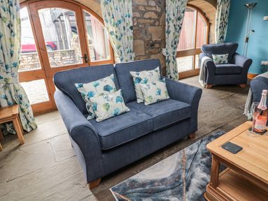 A living room with blue armchairs and loveseat with floral cushions near arched wooden doors at Granary Cottage in Bellingham