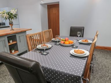 A dining table with polka dot tablecloth set with plates each having a croissant a bowl of fruit and wine glasses in a kitchen at Granary Cottage in Bellingham