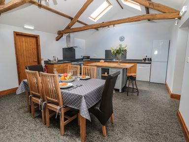 A kitchen and dining area with wooden beams a table set with plates and fruit at Granary Cottage in Bellingham