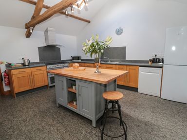 A kitchen with wooden cabinets an island with flowers a stool and appliances at Granary Cottage in Bellingham