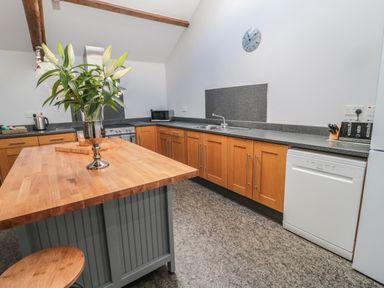 A kitchen with wooden cabinets a wooden island with flowers and appliances at Granary Cottage in Bellingham
