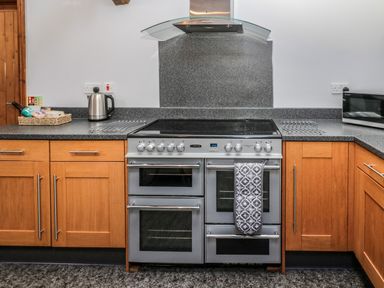 A kitchen with a stainless steel stove and oven set between wooden cabinets with a kettle and microwave on the countertop at Granary Cottage in Bellingham