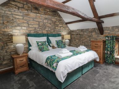 A bedroom with a double bed lamps on wooden bedside tables and stone walls at Granary Cottage in Bellingham