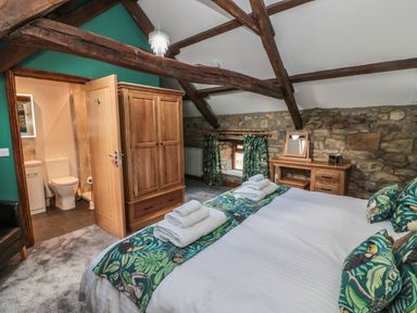 A bedroom with a bed towels wooden wardrobe stone wall and en suite bathroom at Granary Cottage in Bellingham