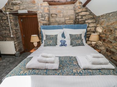 A bedroom with a double bed and patterned blue cushions and bed runner with stacked towels on the foot of the bed at Granary Cottage in Bellingham