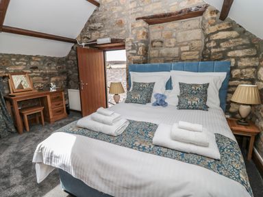 A bedroom with a double bed towels on the bed and exposed stone walls at Granary Cottage in Bellingham