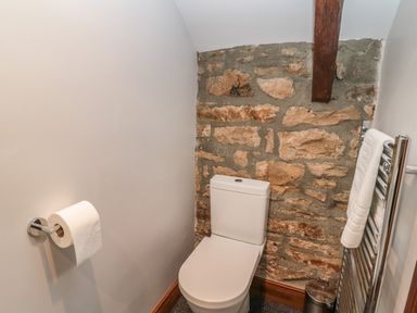 A bathroom with a toilet next to a stone wall and a towel rail at Granary Cottage in Bellingham