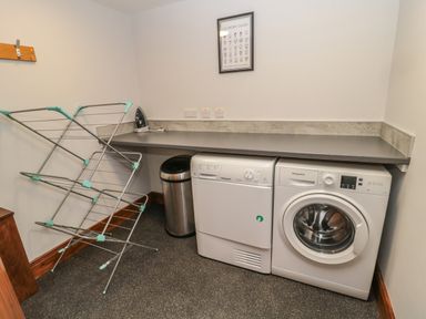 A laundry room with a washing machine dryer ironing board and drying rack at Granary Cottage in Bellingham