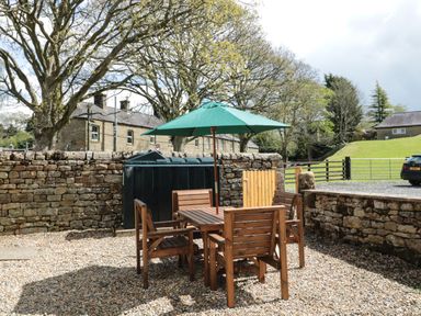 An outdoor patio with a wooden table and chairs under a green umbrella surrounded by stone walls at Granary Cottage in Bellingham