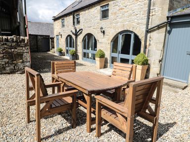 An outdoor stone patio with wooden table and chairs outside a stone building with arched windows at Granary Cottage in Bellingham