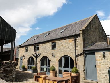 A stone building with arched windows and doors and outdoor wooden furniture at Granary Cottage in Bellingham