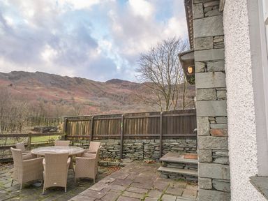 An outdoor patio area with a round table and six chairs next to a stone wall and wooden fence with hills in the background at Plumblands in Chapel Stile
