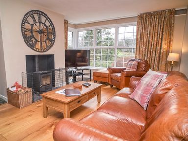 A living room with leather sofa and armchair a wooden coffee table a large wall clock and a television by the window at Plumblands in Chapel Stile