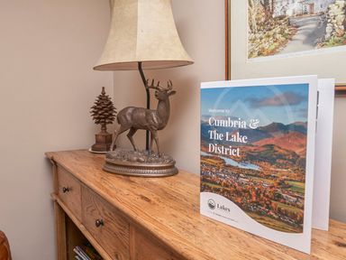 A wooden sideboard with a lamp a metal deer sculpture a pinecone ornament and a folder about Cumbria and The Lake District at Plumblands in Chapel Stile