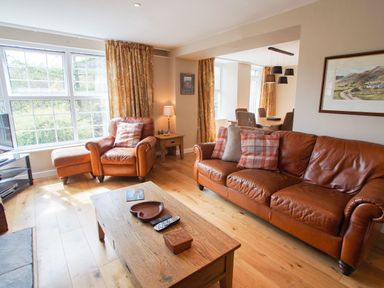 A living room with a leather armchair and sofa a wooden coffee table and large windows at Plumblands in Chapel Stile
