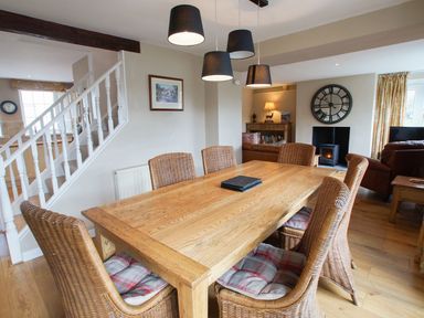 A dining area with a wooden table and wicker chairs near a staircase and a living room with a fireplace at Plumblands in Chapel Stile