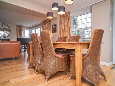 A dining area with a wooden table and wicker chairs next to windows with floral curtains at Plumblands in Chapel Stile