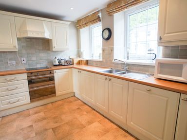 A kitchen with white cabinets a double sink a microwave toaster kettle and oven at Plumblands in Chapel Stile