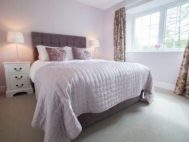 A bedroom with a bed with pillows bedside tables with lamps and a window with floral curtains at Plumblands in Chapel Stile