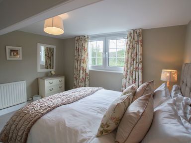 A bedroom with a bed with cushions and blanket a chest of drawers a mirror a lamp and curtains at Plumblands in Chapel Stile