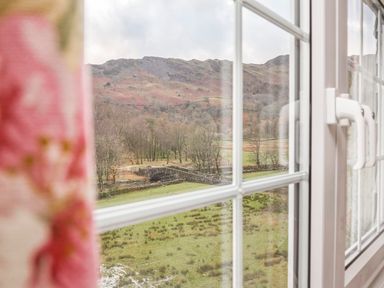 A landscape view of hills trees and a stone bridge seen through a window with a floral curtain at Plumblands in Chapel Stile