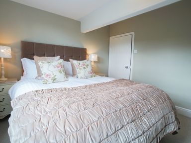 A bedroom with a large bed floral pillows nightstands and lamps at Plumblands in Chapel Stile
