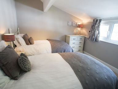 A bedroom with two single beds bedside table lamp chest of drawers and window with curtains at Plumblands in Chapel Stile
