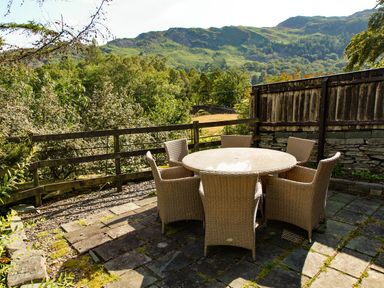 An outdoor patio with a round table and six wicker chairs overlooking trees and hills at Plumblands in Chapel Stile