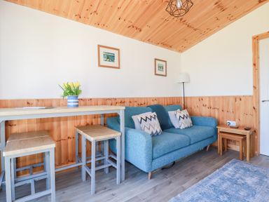 A living room with a blue sofa table and stools with flowers on the table at 194 Atlantic Bays in Atlantic Bays Holiday Park near St Merryn