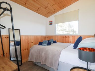 A bedroom with a bed towels a standing mirror wooden ceiling and window at 194 Atlantic Bays in Atlantic Bays Holiday Park near St Merryn
