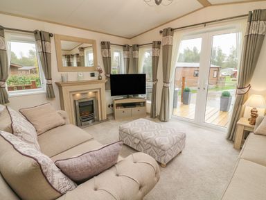 A living room with sofas a fireplace a television and glass doors at Lancaster Lodge in South Lakeland Leisure Village