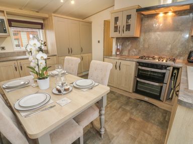 A kitchen with a dining table set for four with plates and wine glasses and an orchid plant at Lancaster Lodge in South Lakeland Leisure Village