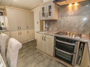 A kitchen with cabinets a gas stove an oven and dining chairs at Lancaster Lodge in South Lakeland Leisure Village