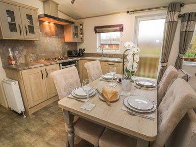 A kitchen and dining area with a round dining table set for four including plates wine glasses and a loaf of bread at Lancaster Lodge in South Lakeland Leisure Village