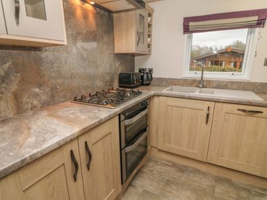 A kitchen with wooden cabinets a gas stove an oven a sink and a window with a view at Lancaster Lodge South Lakeland Leisure Village