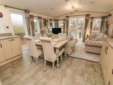 A living room and dining area with a dining table set for four chairs and sofas near windows at Lancaster Lodge in South Lakeland Leisure Village