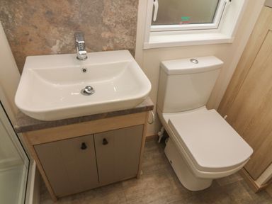 A bathroom with a sink on a cabinet next to a toilet under a window at Lancaster Lodge South Lakeland Leisure Village