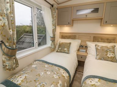 A bedroom with two single beds separated by a nightstand under cabinets at Lancaster Lodge South Lakeland Leisure Village