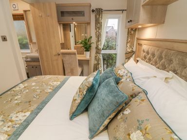 A bedroom with a bed with floral pillows and a small writing desk with a plant at Lancaster Lodge South Lakeland Leisure Village