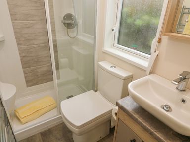 A bathroom with a shower, toilet, sink, window, and yellow towel at Lancaster Lodge in South Lakeland Leisure Village